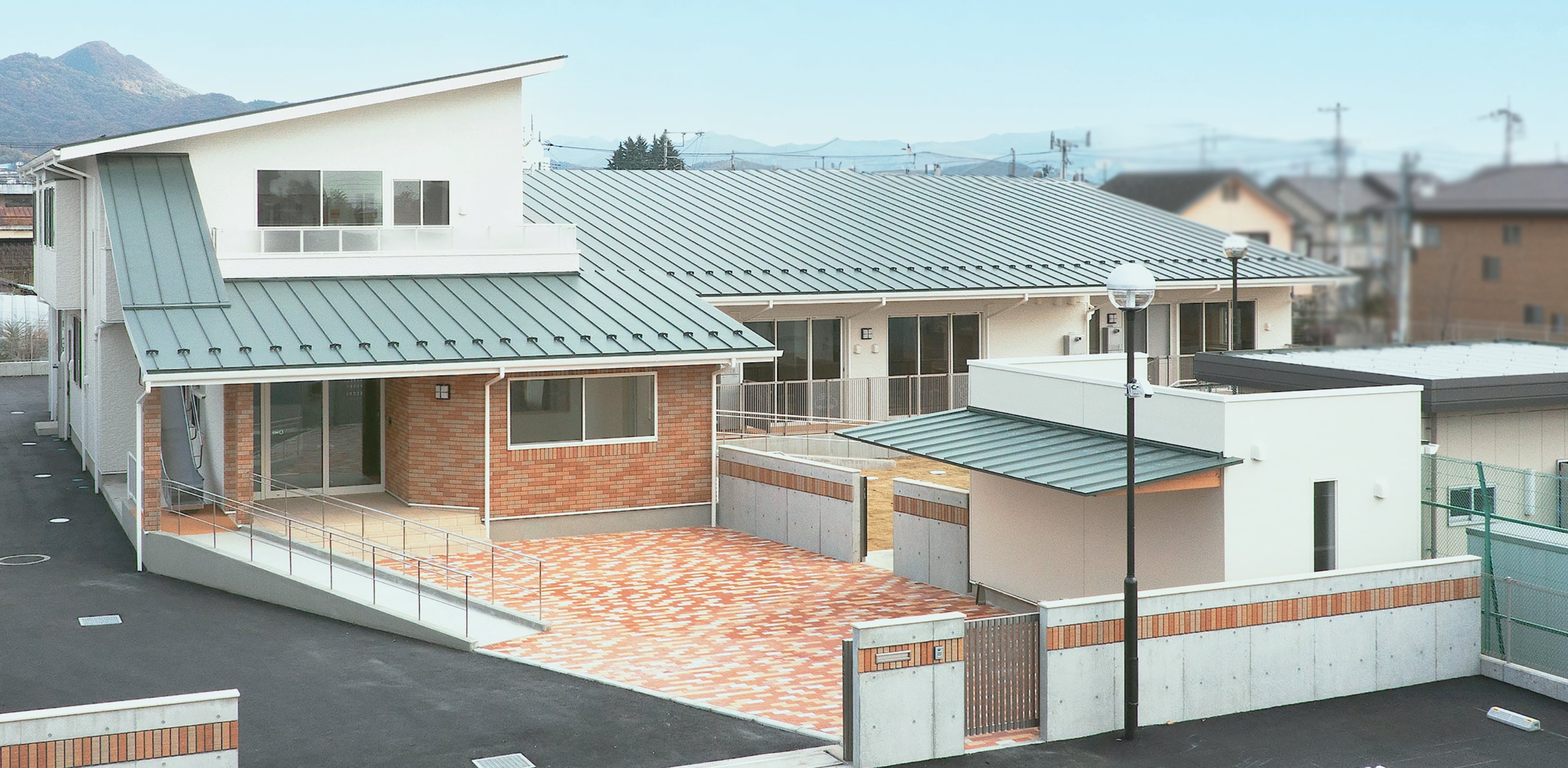 桐育乳児園は屋根が緑で壁が白色の園舎です。駐車スペースも複数あります。